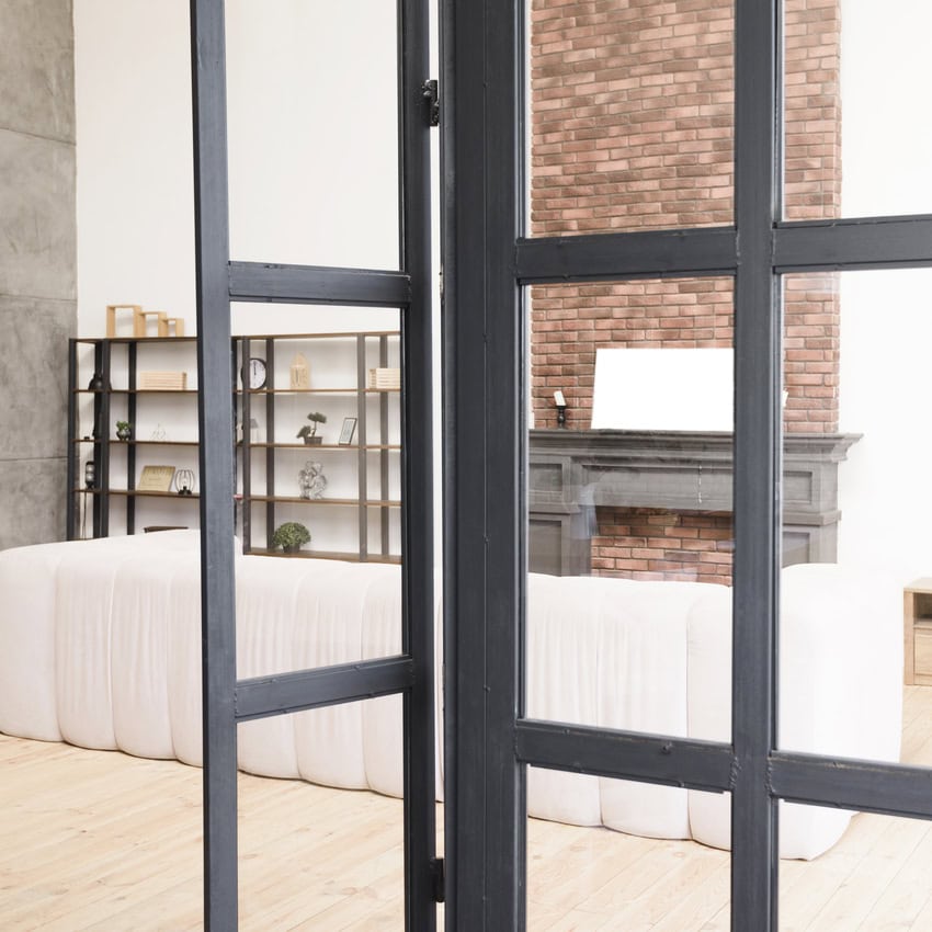 Reforma integral d'una sala d'estar moderna té una paret d'accent de maó, terres de fusta clara, un sofà blanc i prestatgeries elegants, un testimoni de la finor integral de reforma. Les portes de vidre emmarquen meravellosament la vista.