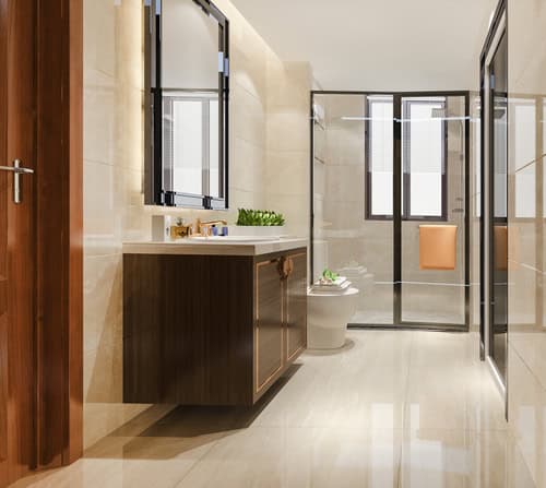 Rehabilitació bany modern amb parets i terres de rajola beix disposa d'un lavabo de fusta amb mirall, dutxa amb tancament de vidre i lavabo. Una petita planta en test es troba prop de la pica, afegint un toc de natura a aquest elegant espai integral reformat.